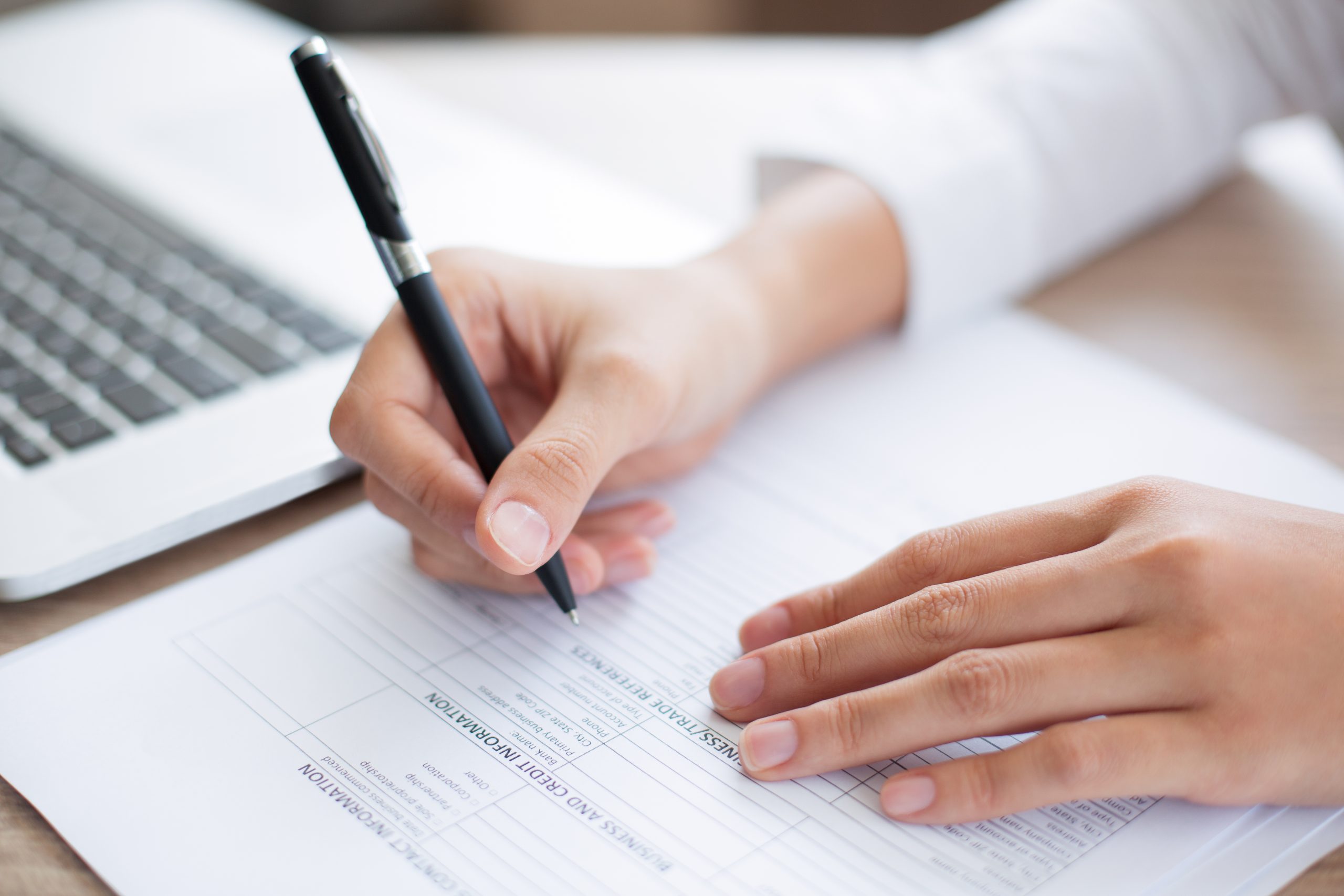 Cropped view of person holding pen and filling out application form on table